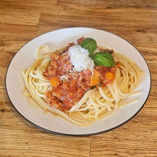 Cooked spaghetti with ragú, topped with parmesan and basil leaves
